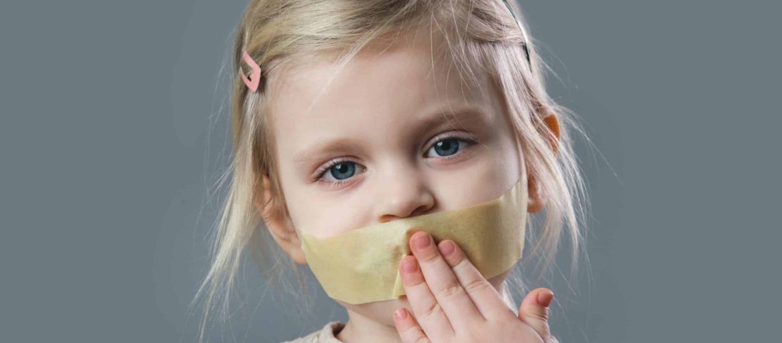 Studio portrait of adorable little girl with adhesive tape over her mouth. Little girl with no voice, freedom of speach or  forbidden opinion concept.